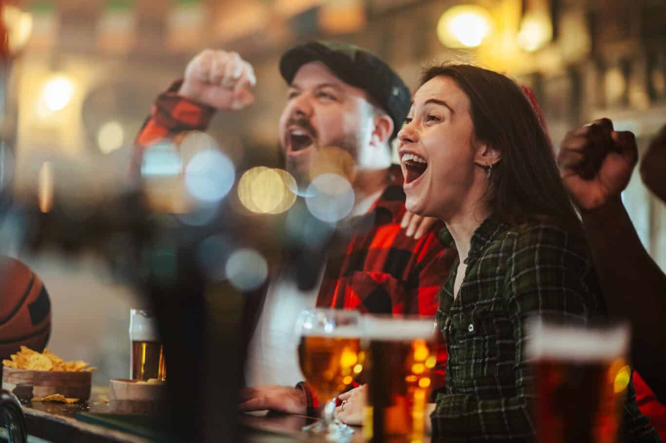 Friends cheering and celebrating while watching a sports game in a lively bar, showing excitement and unity