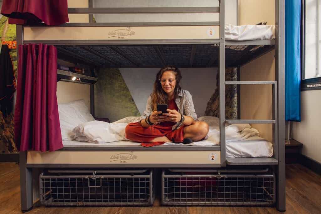 Female guest sitting on bunk bed in Mitte Hostel Berlin, using her phone.