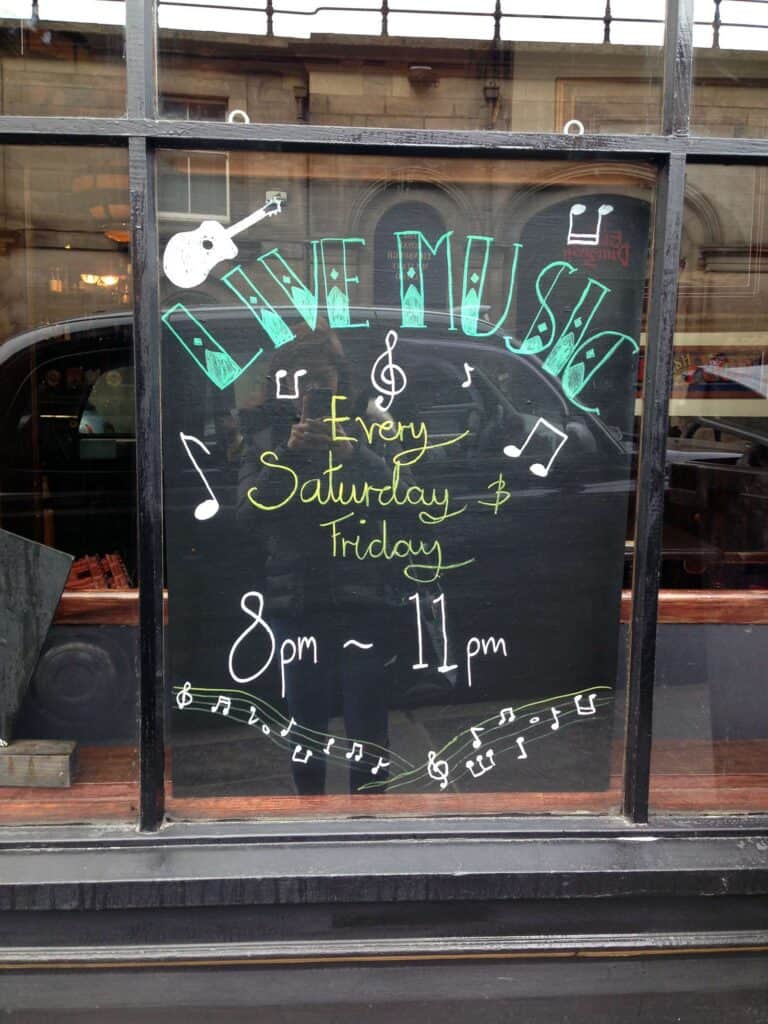 Live music event sign at Mitte Hostel, Berlin, featuring guitar and musical notes.