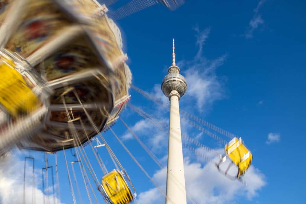 Bright view of Berlin TV Tower with a nearby amusement park ride in the foreground.