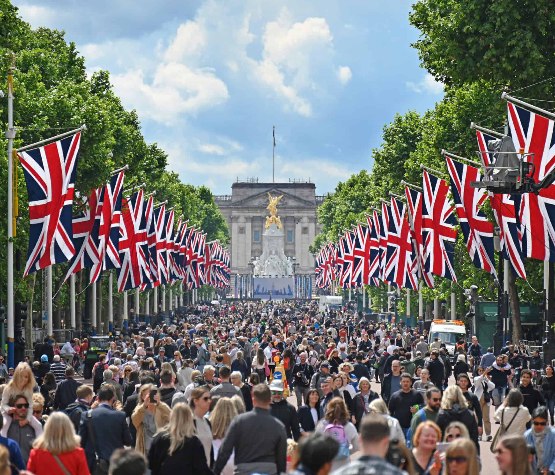 London street with Union Jack flags and a large crowd near Buckingham Palace.