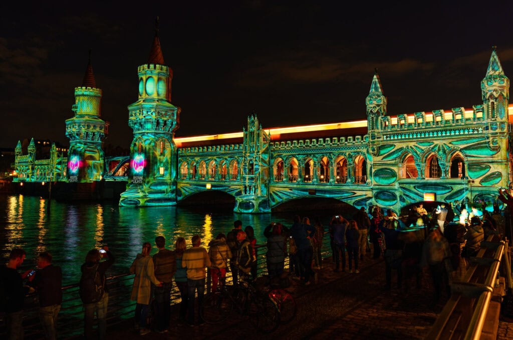 Night view of illuminated Oberbaum Bridge in Berlin with people enjoying the scene.