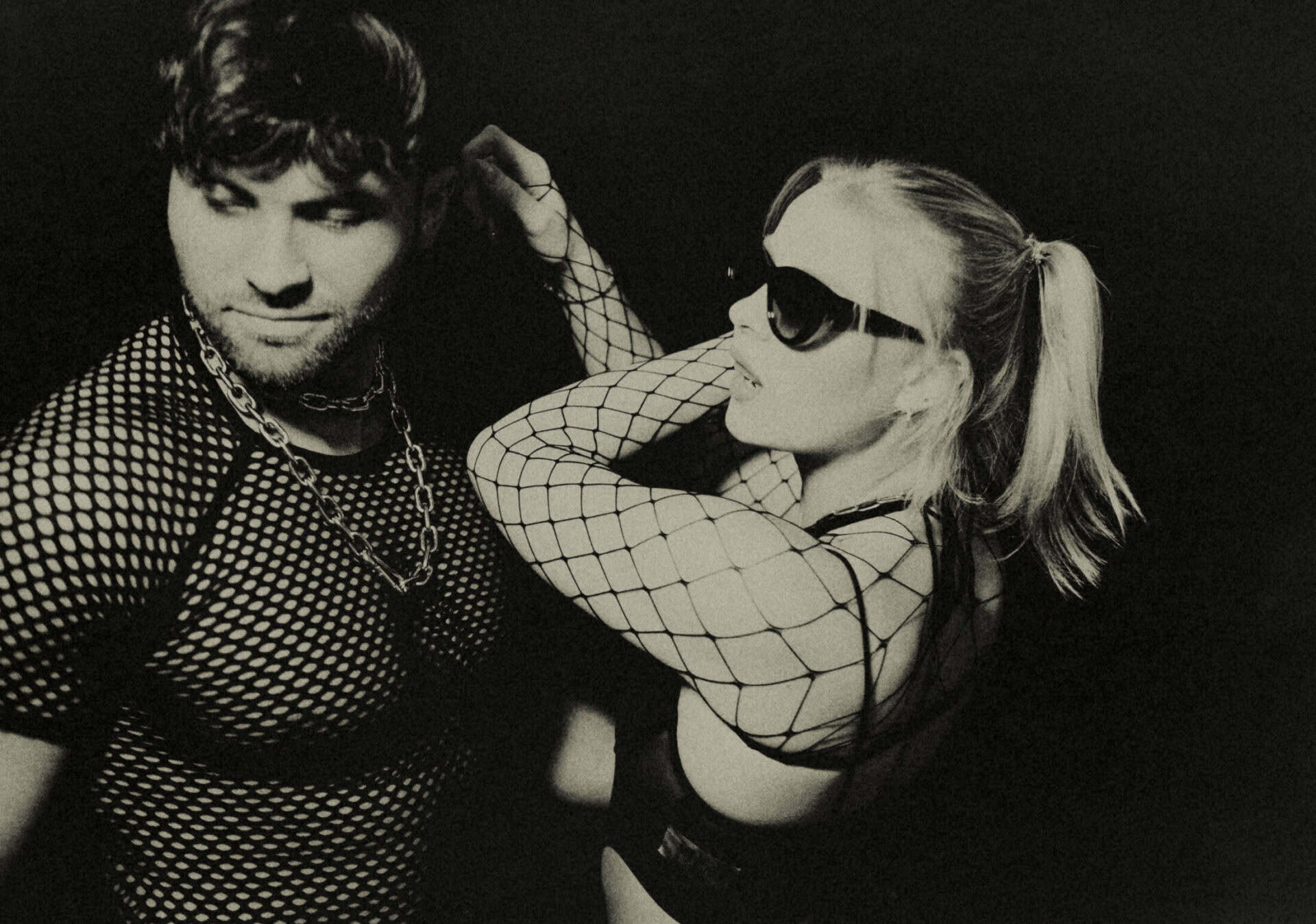 Stylish young woman in sunglasses and fishnet top with a man in a patterned shirt, enjoying Berlin’s.
