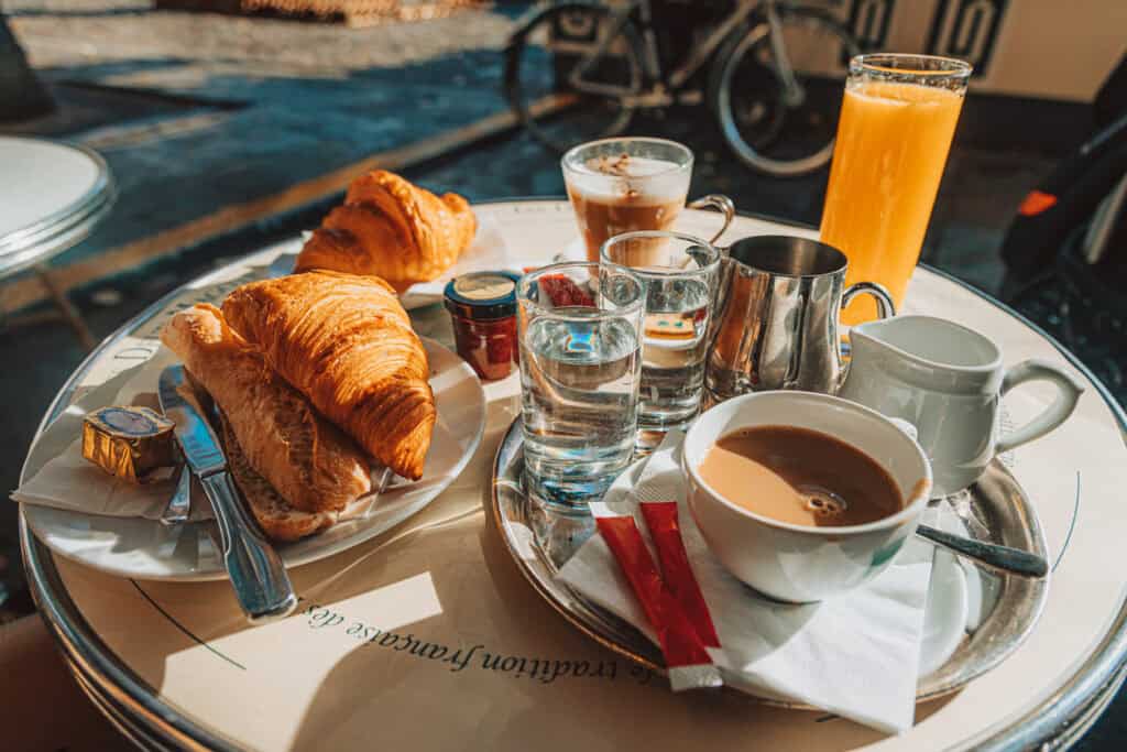 A breakfast table featuring croissants, coffee, orange juice, and tea at a sunny Berlin café.