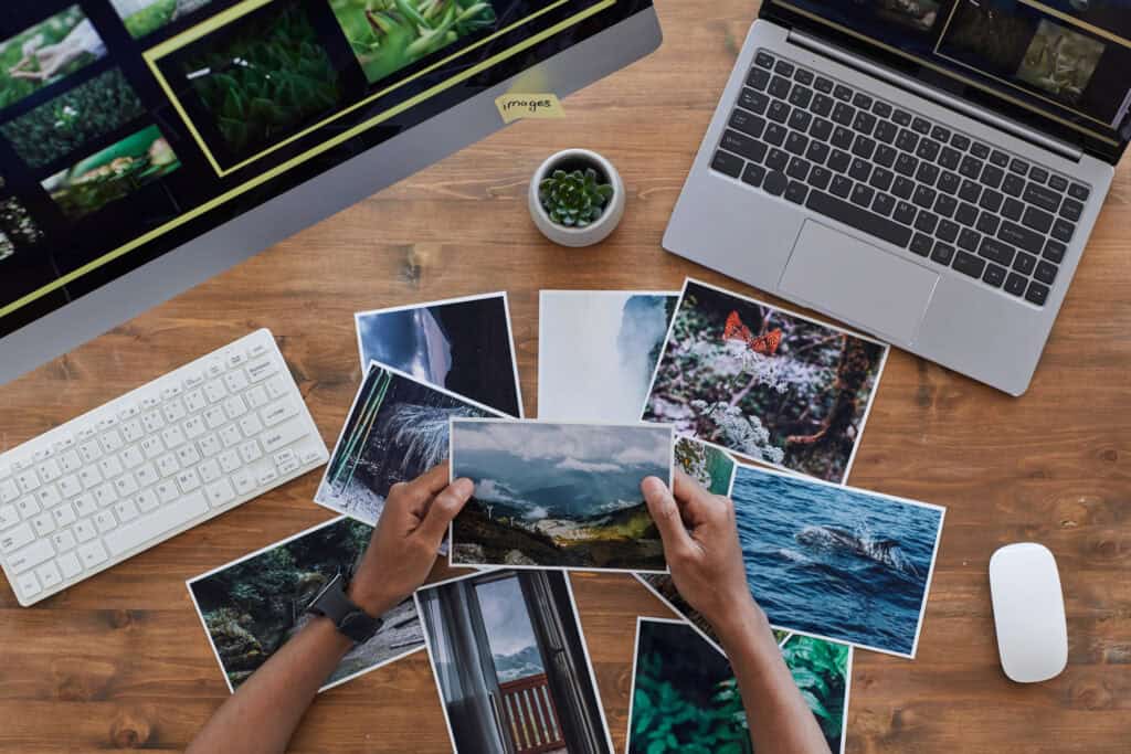 Photographer reviewing travel photos at a desk with laptop and computer monitor.