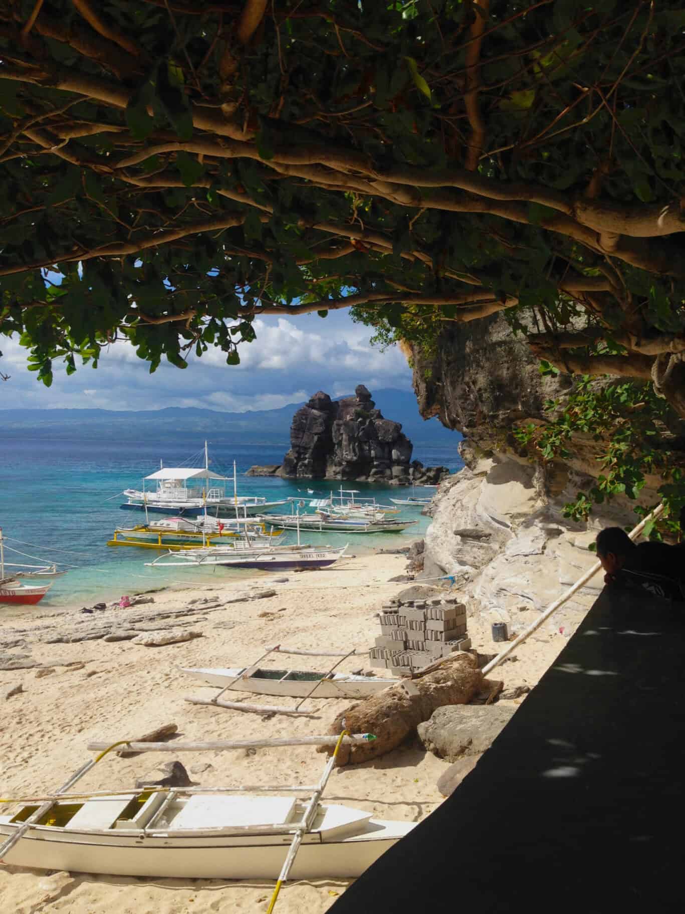 Beach scene with boats, rocky cliffs, and lush greenery in a tropical setting.