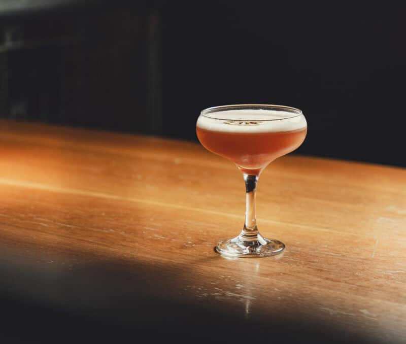 Cocktail in a coupe glass on a wooden bar counter.