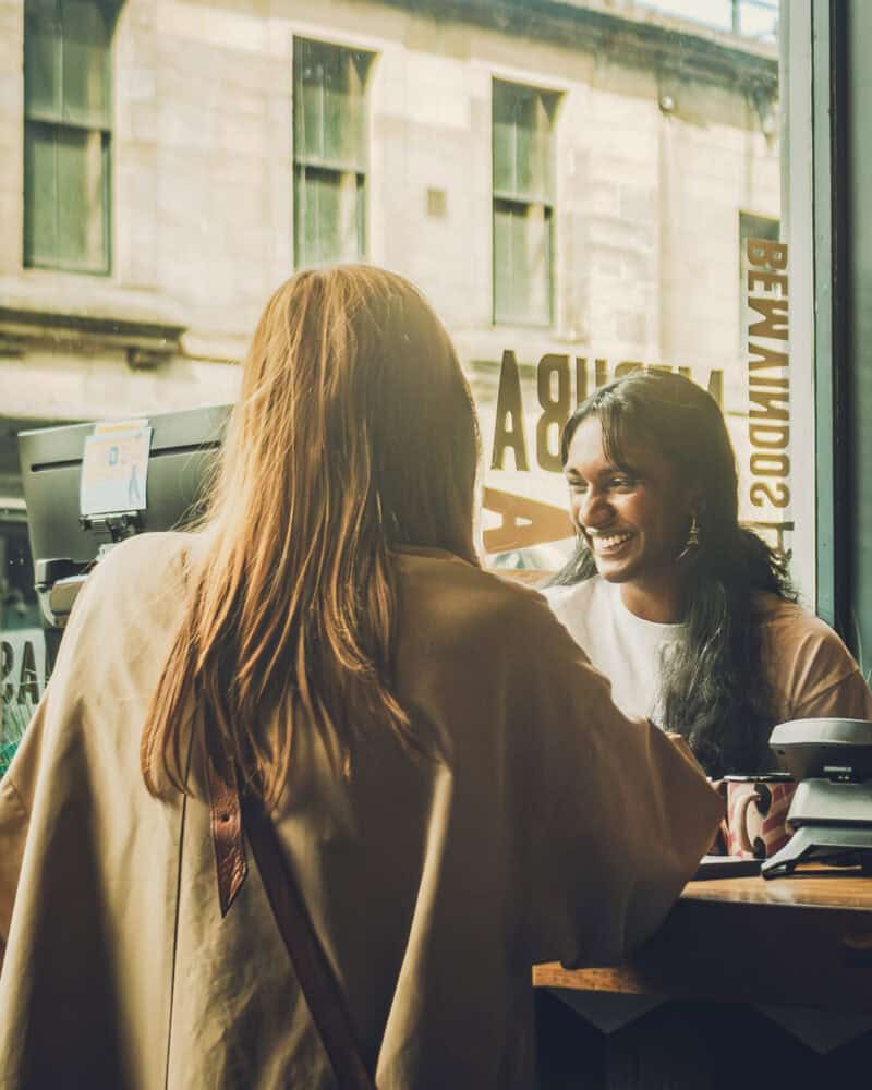 Interior view of two women smiling and chatting inside St Christopher's café.